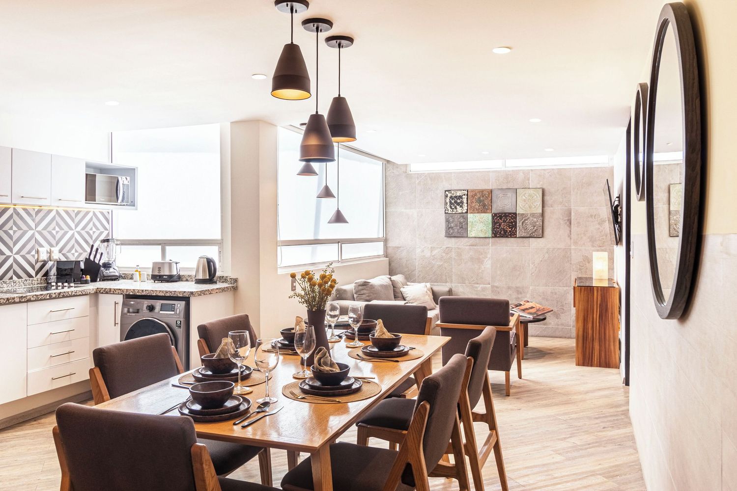 Modern open concept kitchen and dining area with pendant lights, wood floors, and minimalist decor in neutral tones.