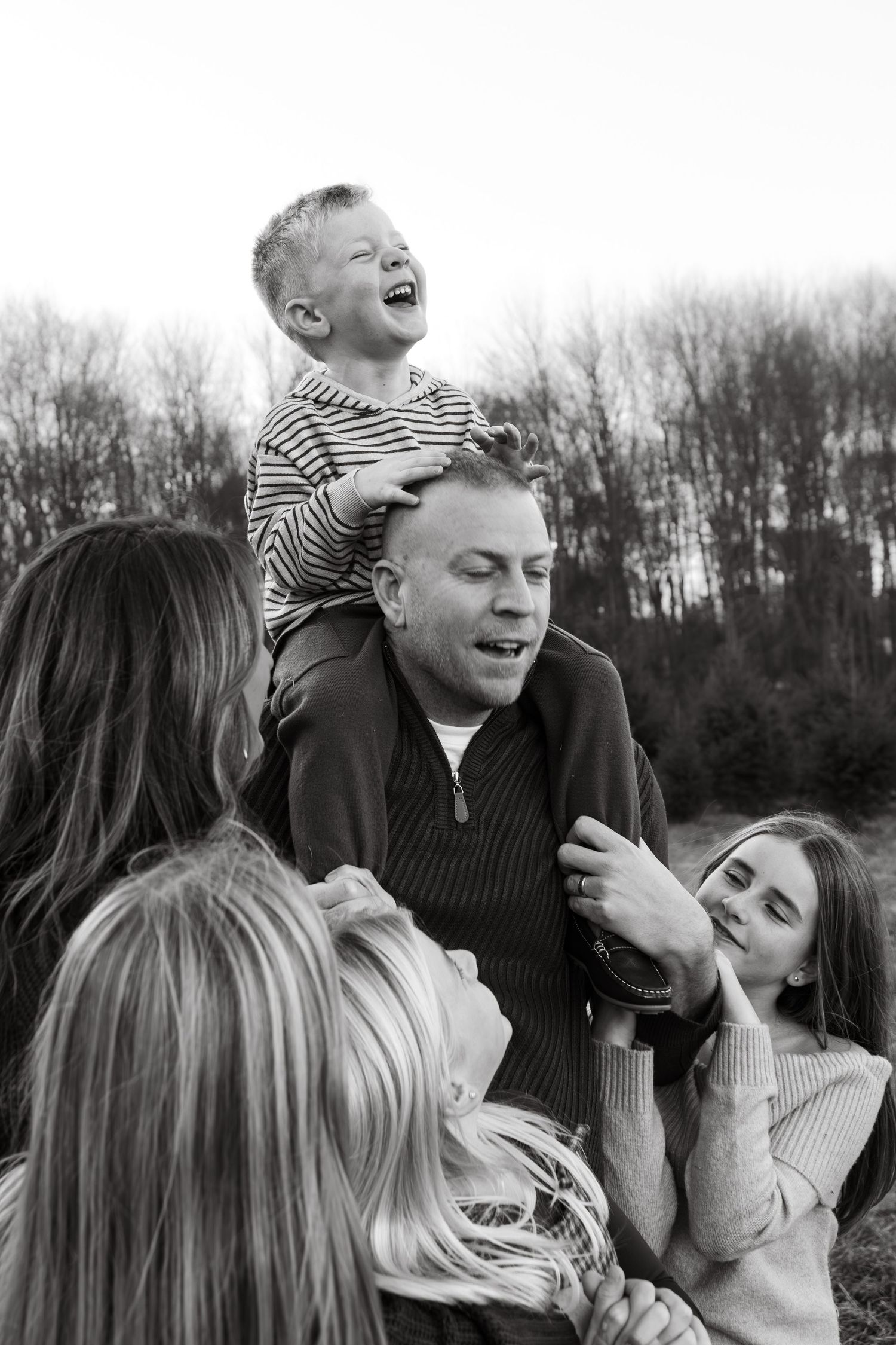 A black and white photo sequence showing a playful family of 6 outdoors with joyful expressions and natural scenery during mini photoshoot.