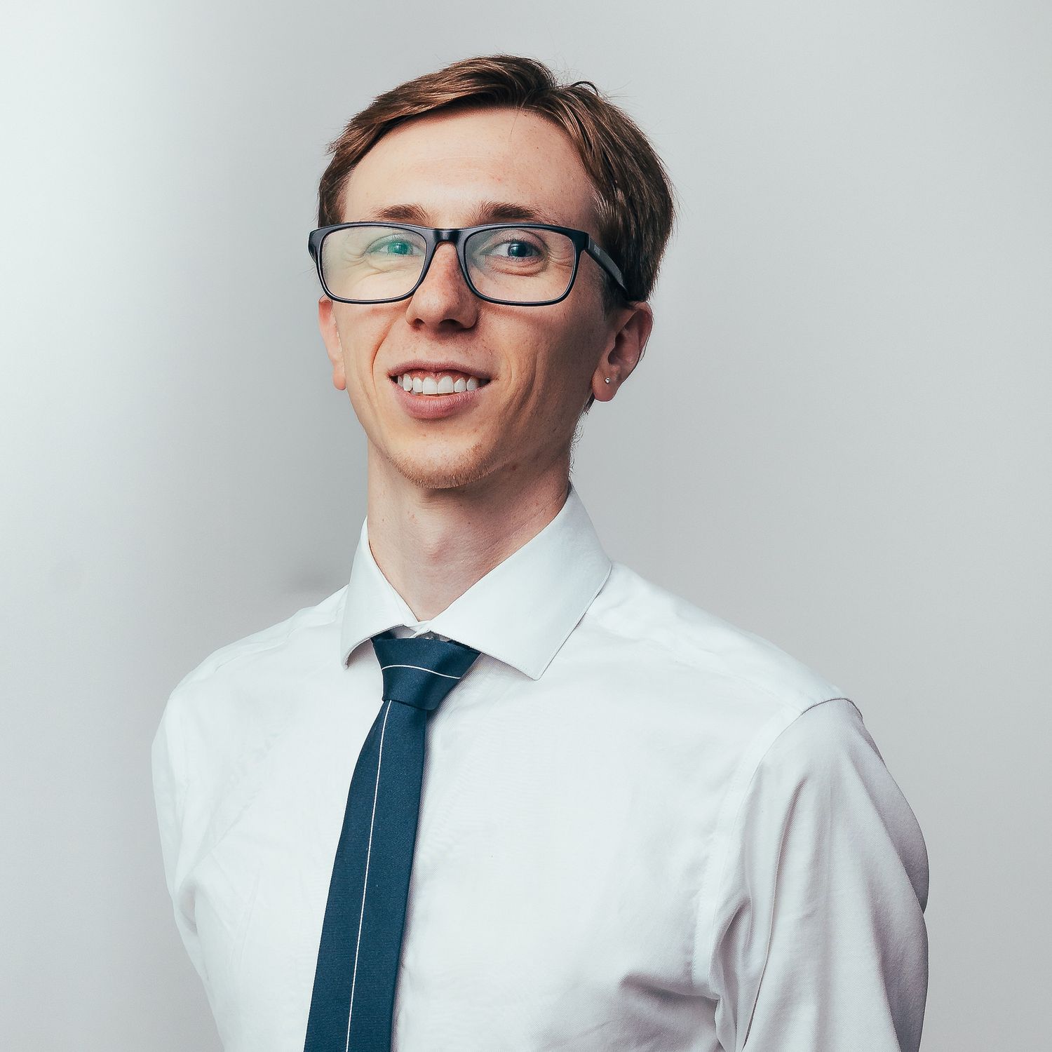 Professional wearing a white dress shirt and blue tie smiles while posing against a light background.