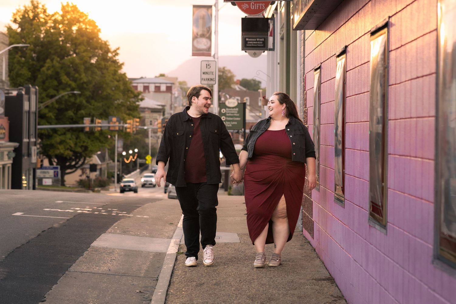 People walk past a pink-painted building exterior during golden hour lighting on an urban street.