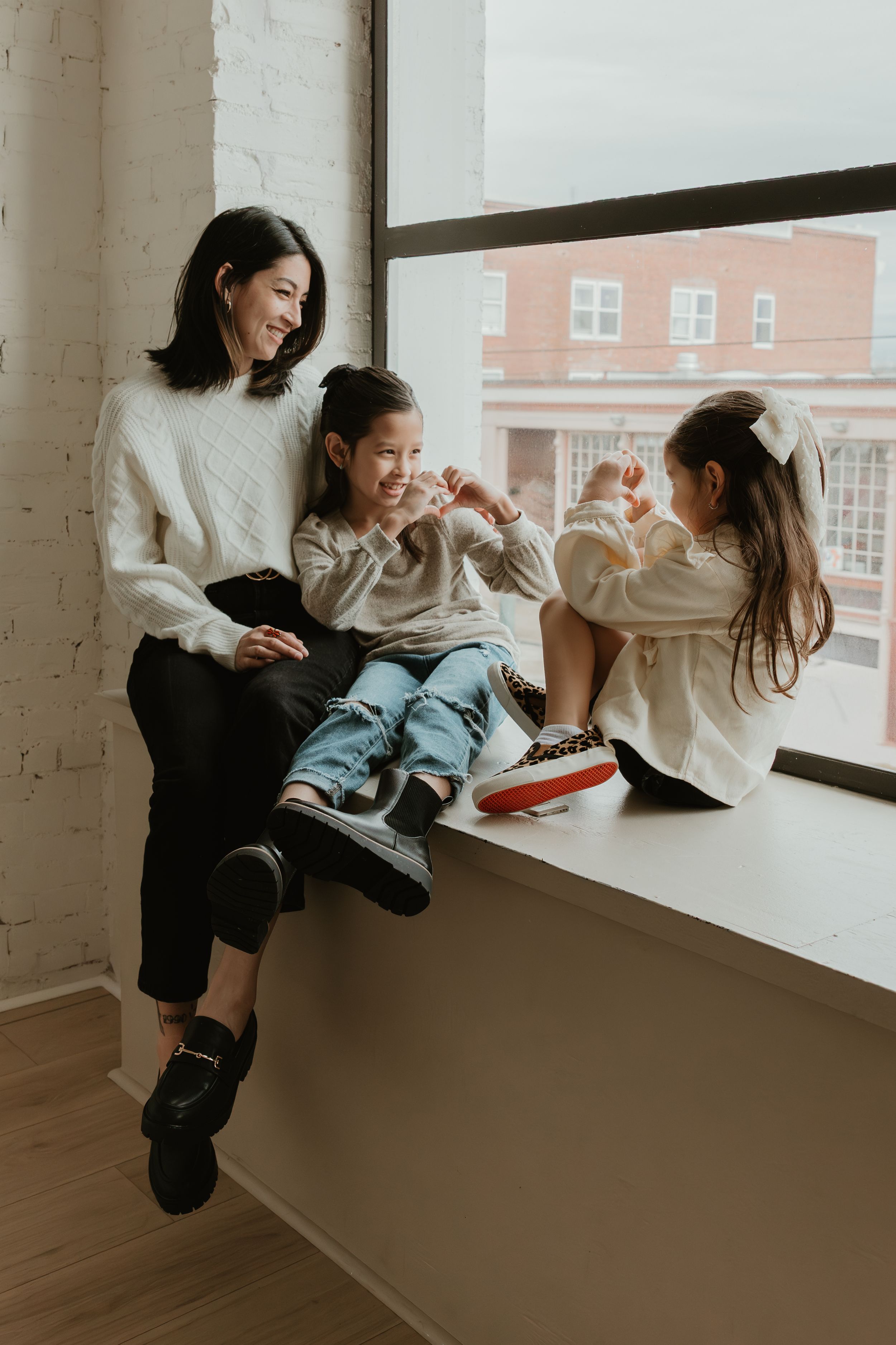 Person in white sweater and jeans sits casually by window ledge in minimalist indoor setting with natural light.