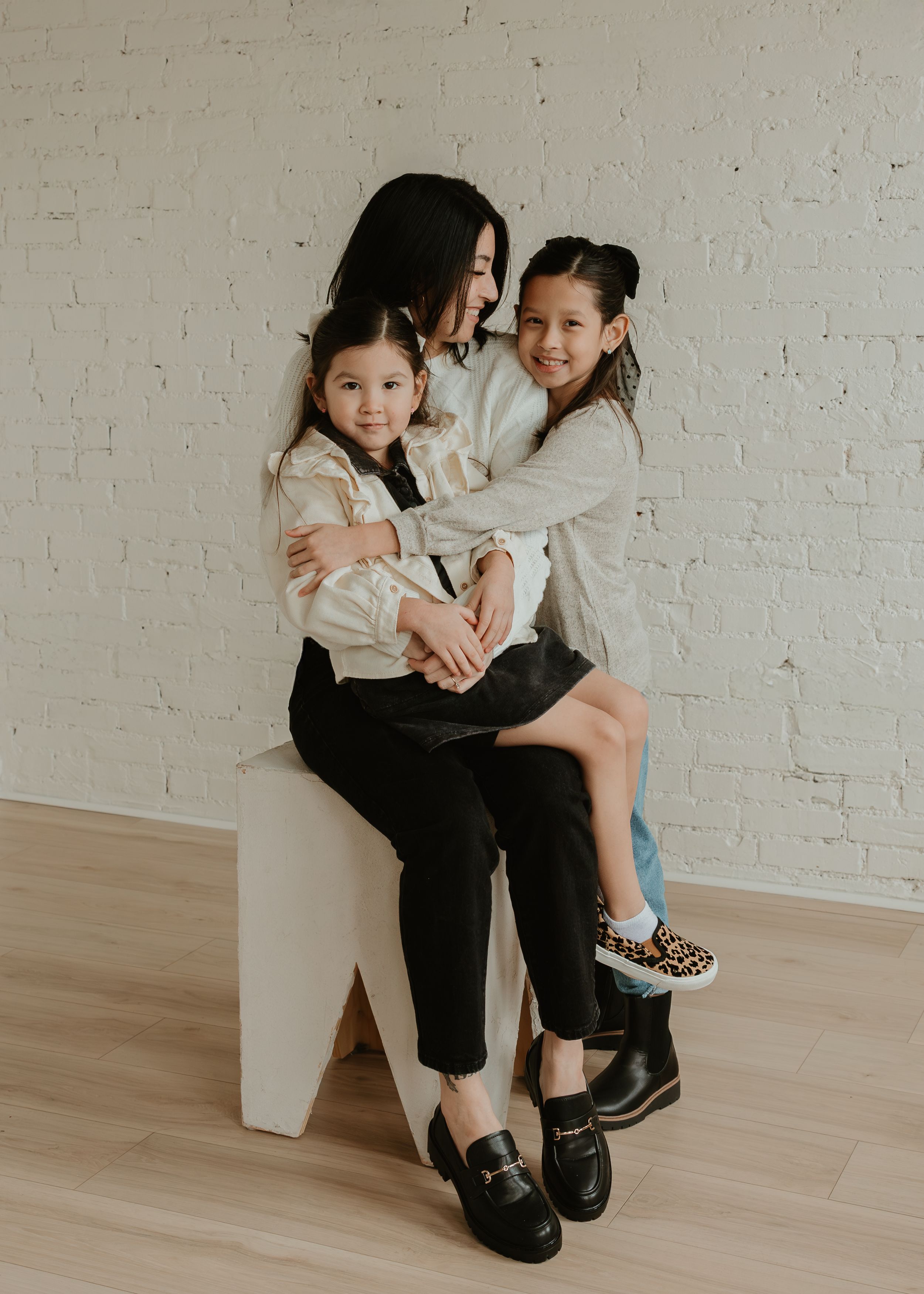 Parent and child share tender moments together against white brick wall and light wood flooring.
