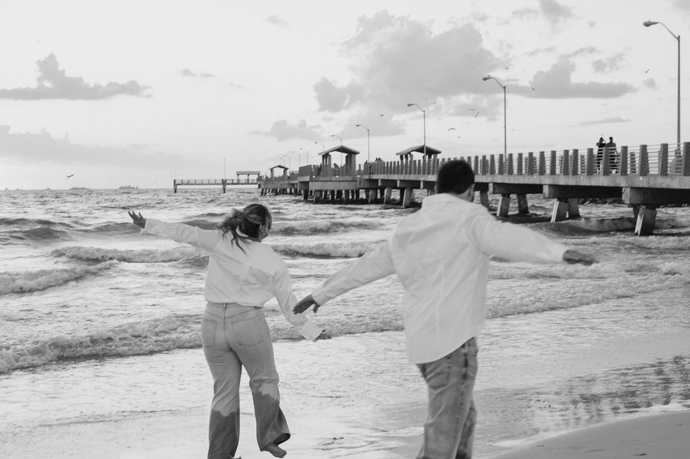 Couple walking along a beach pier during sunset in black and white.