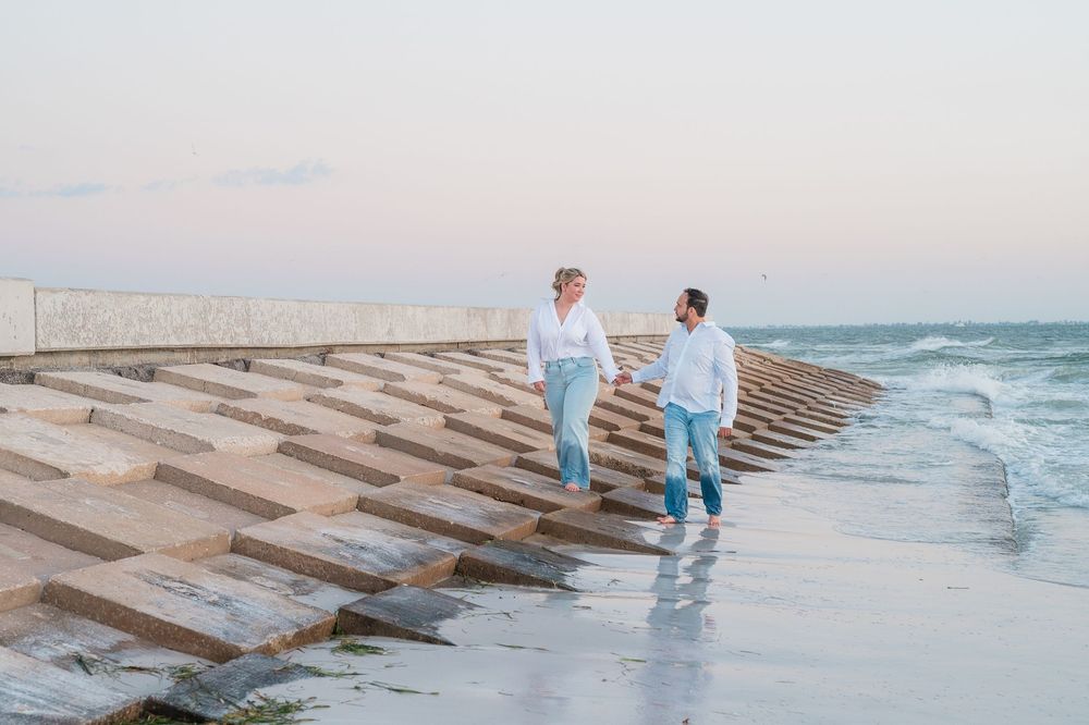 Couple walking on geometric concrete breakwater along ocean shore during sunset.