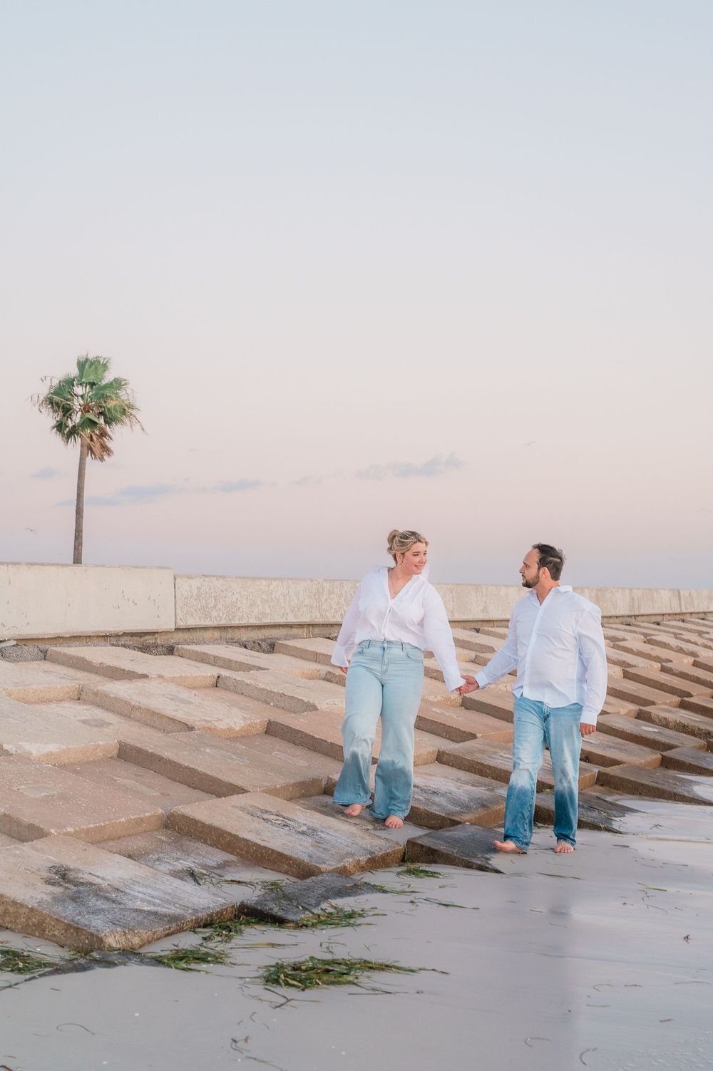 Two people in coordinated blue and white outfits sit together on geometric concrete steps near the ocean.