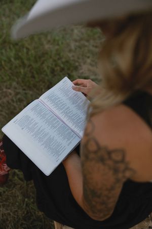 Person reading a book while lying in grass on a sunny day.