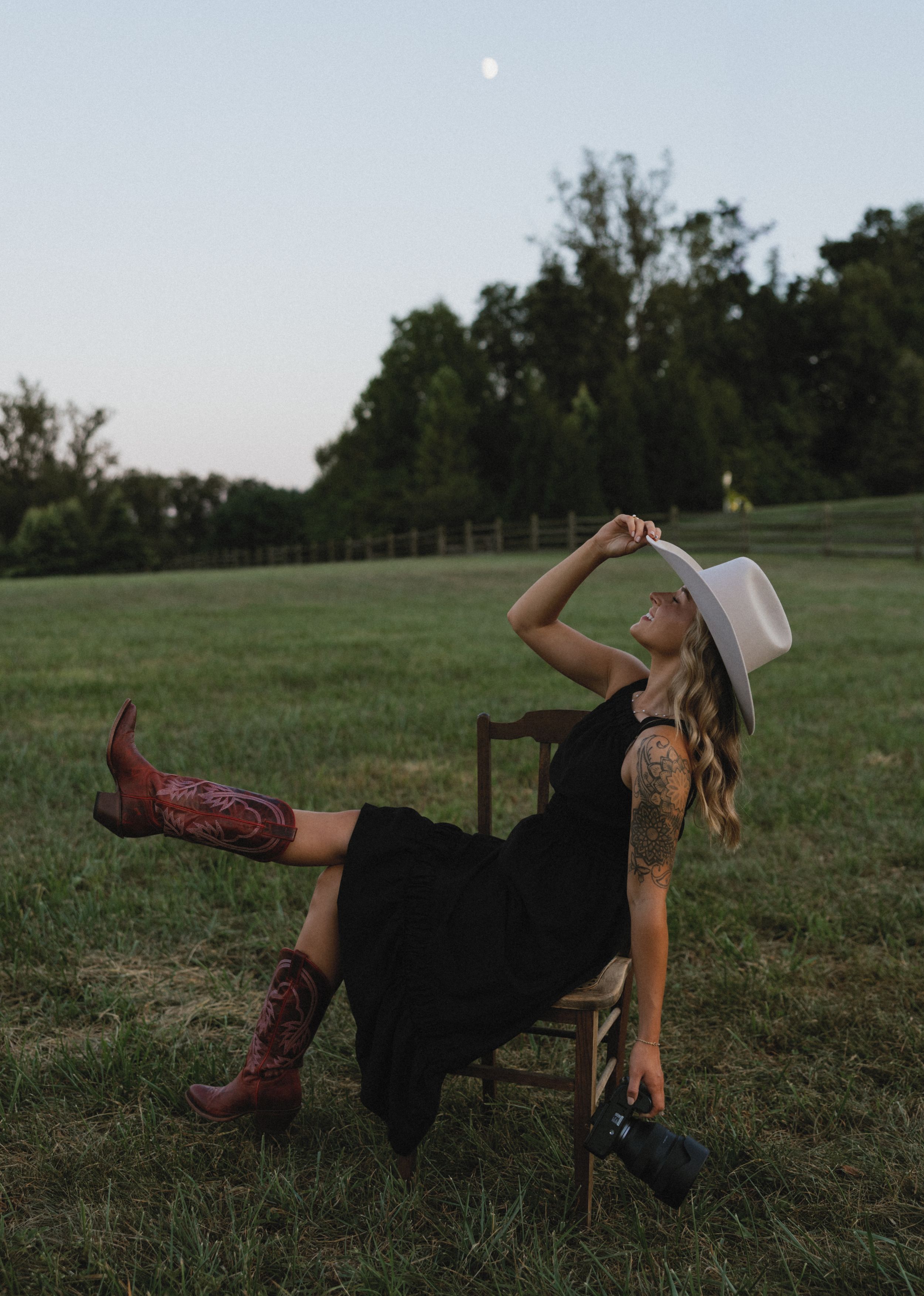 Person in black dress and boots relaxing on grassy field at sunset.