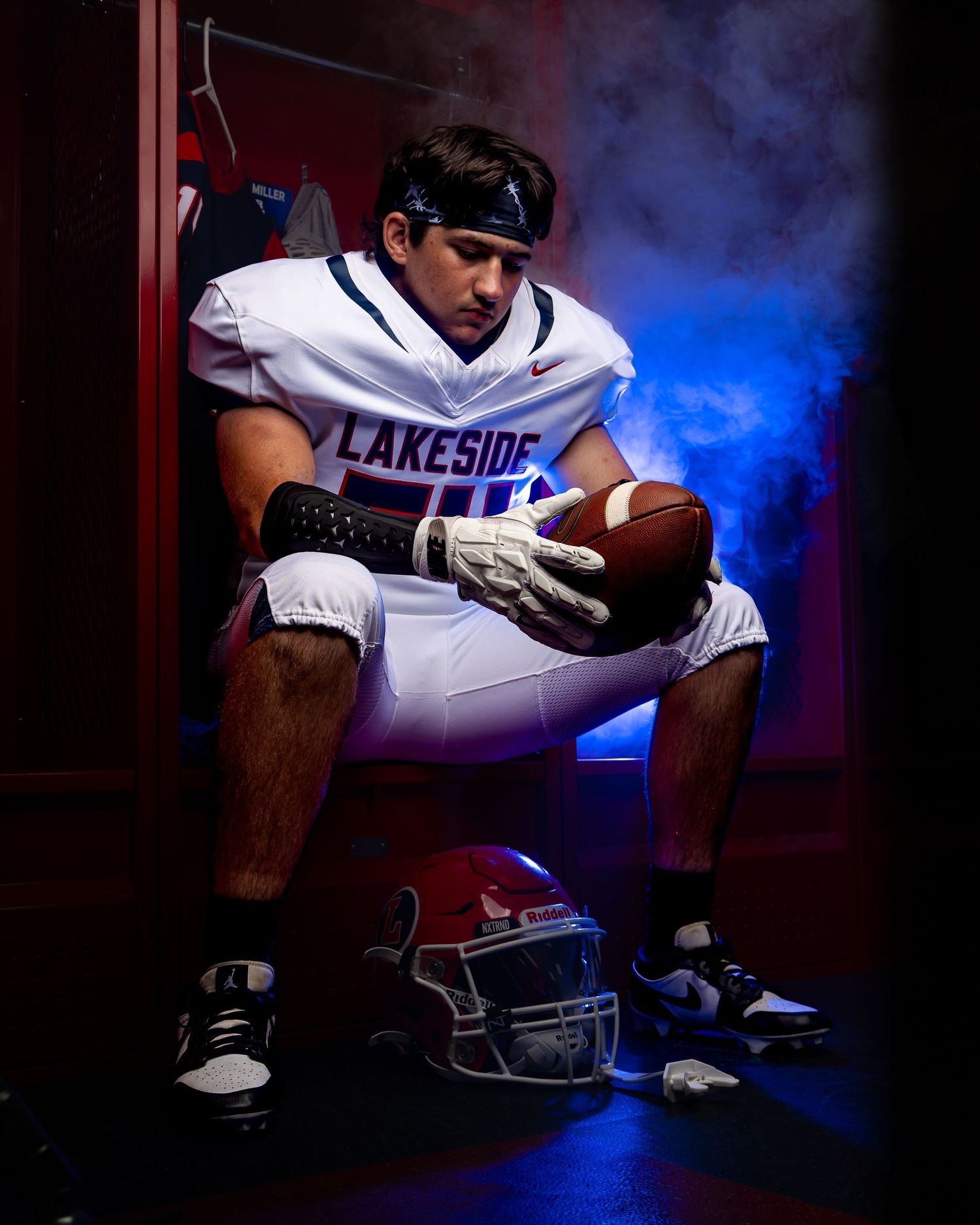 A dramatic sports portrait featuring a football player's hands and helmet silhouetted against moody blue lighting effects.