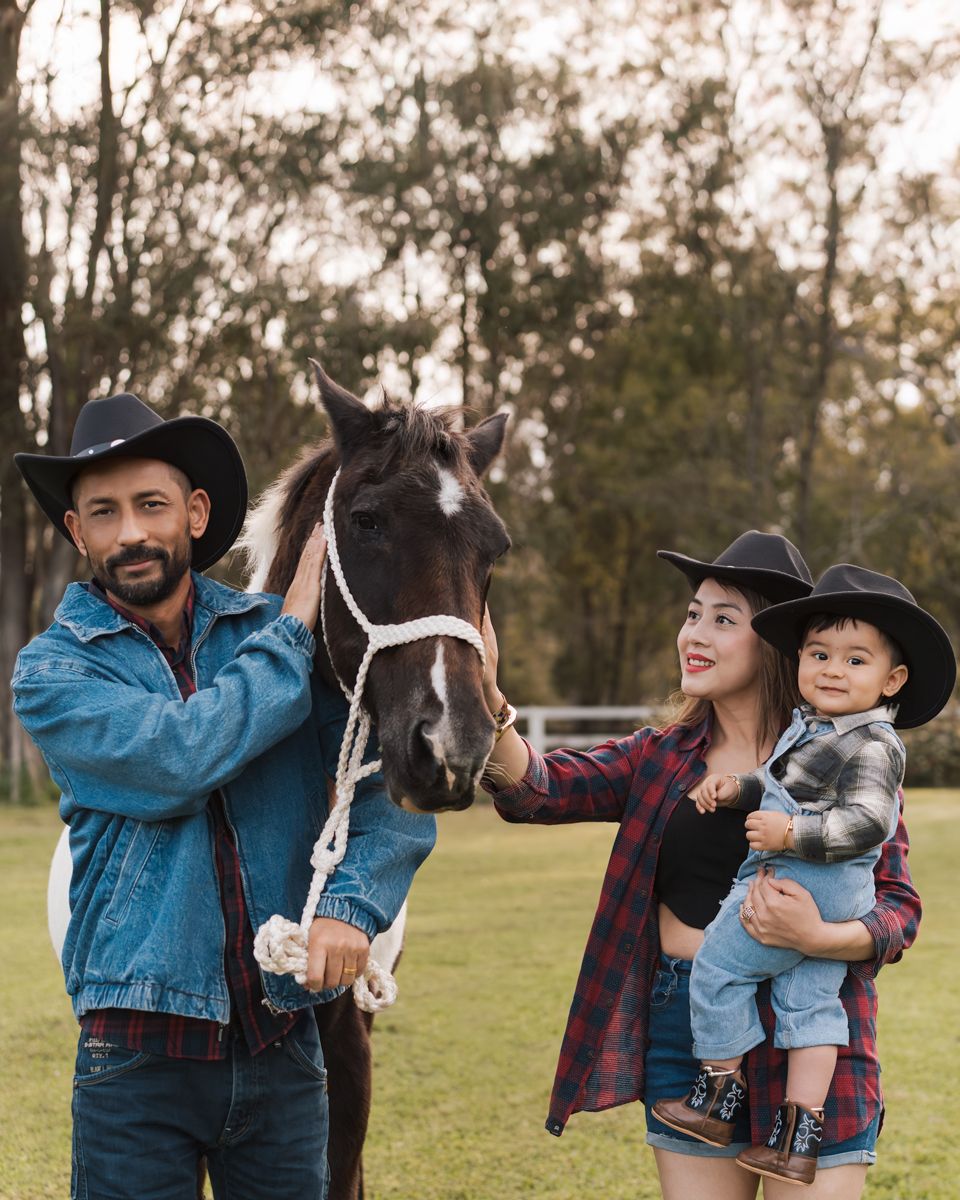 western style family smiling together in an outdoor grassy field at sunset with their one year old little boy & horse photoshoot