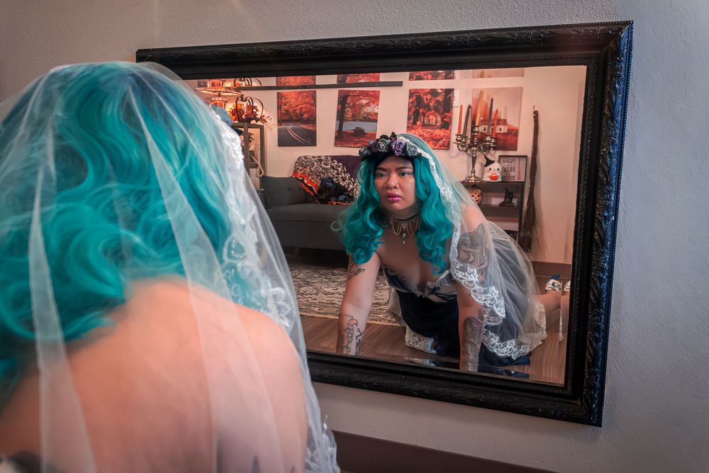 A reflection in a mirror shows someone wearing a veil and crawling towards a mirror with artwork on the wall behind them.