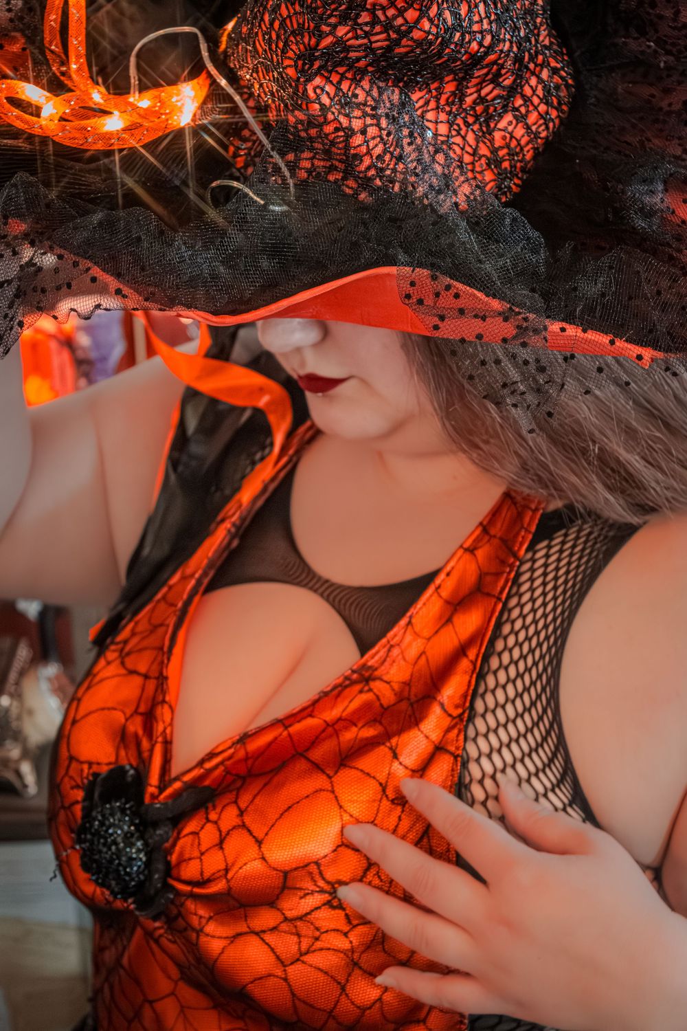 Close-up shot in orange lighting showing spiderweb-patterned lingerie details.