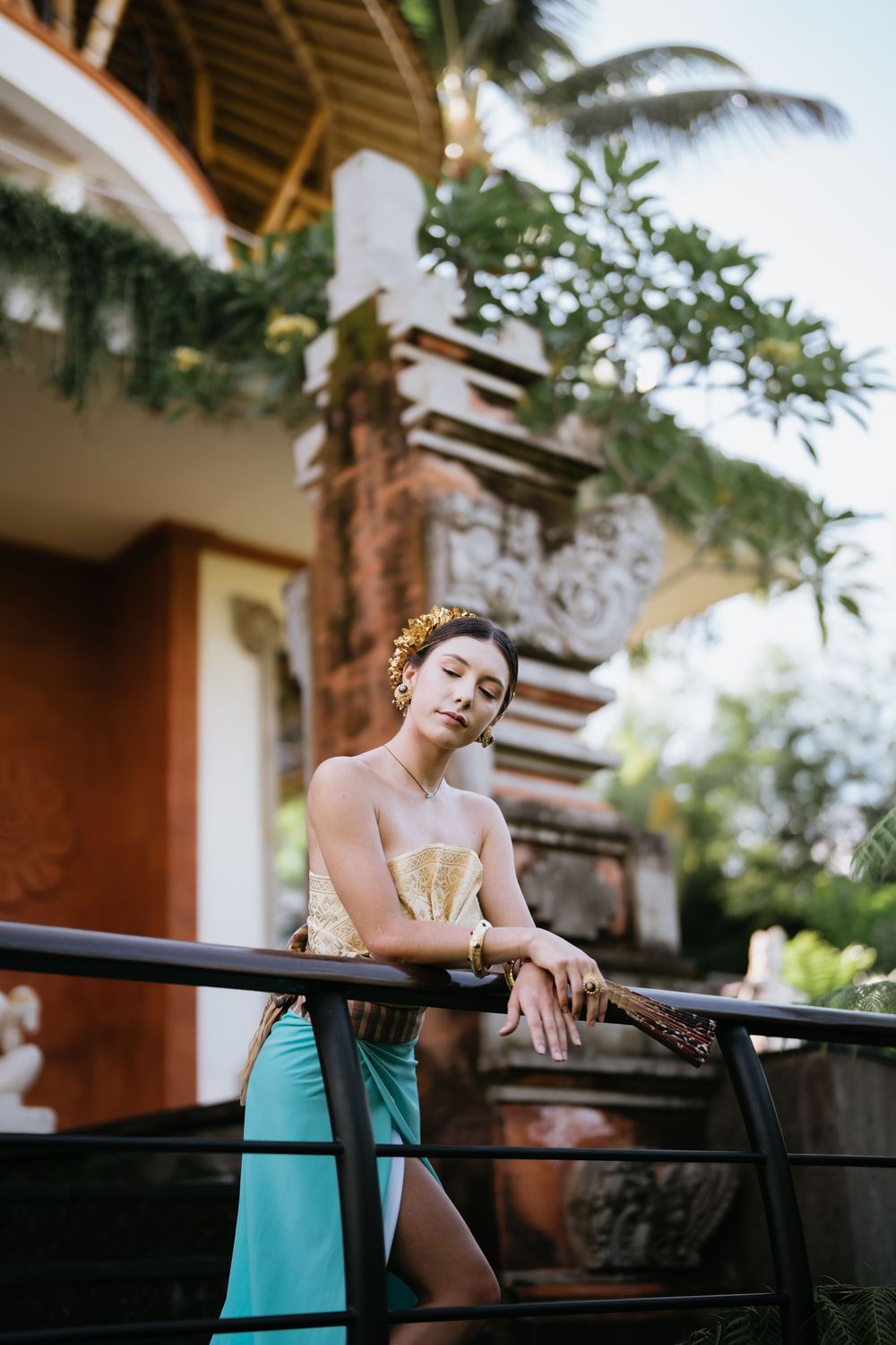 Elegant portrait against Balinese architecture with turquoise sarong and gold accessories.