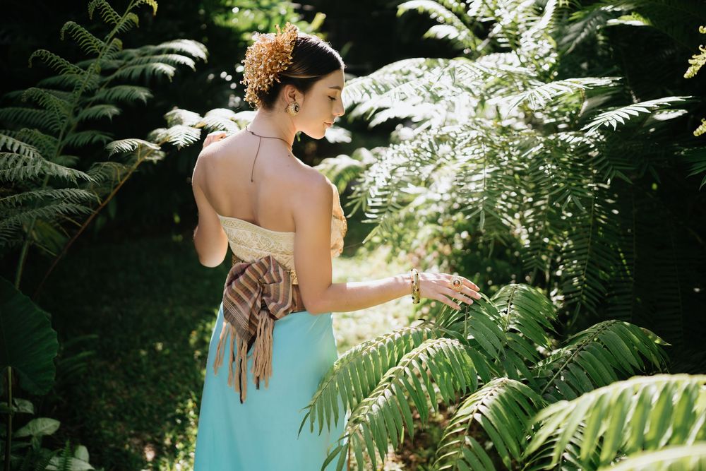 Back view of traditional costume with teal sarong among tropical ferns.