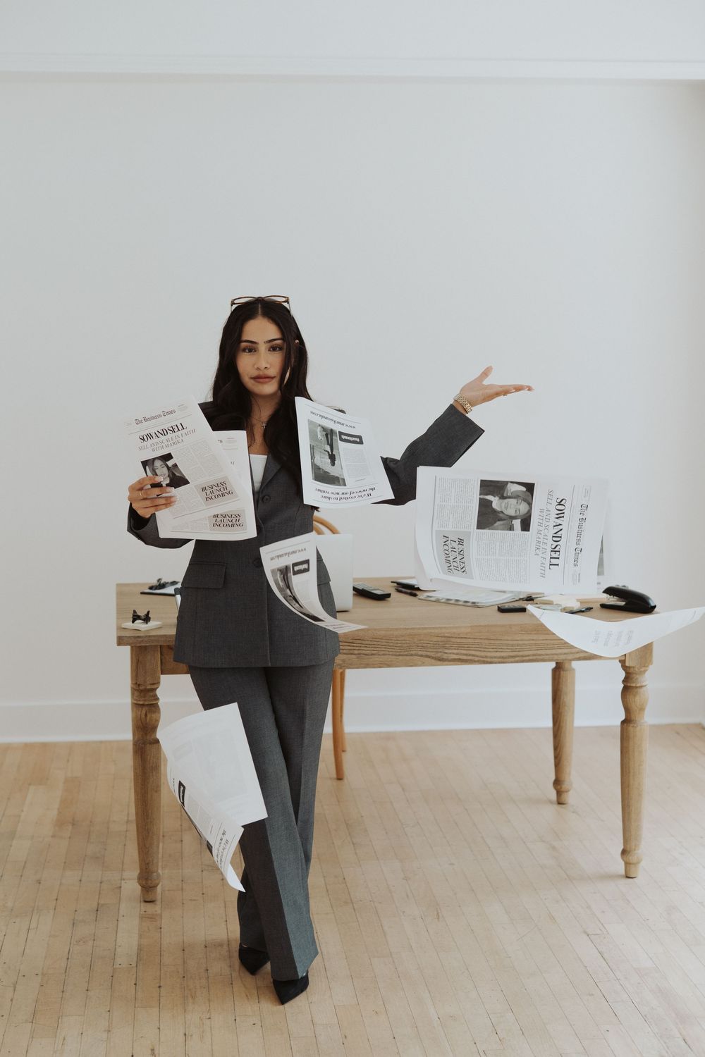 Professional in business attire standing by a wooden table with papers in a minimalist white room.
