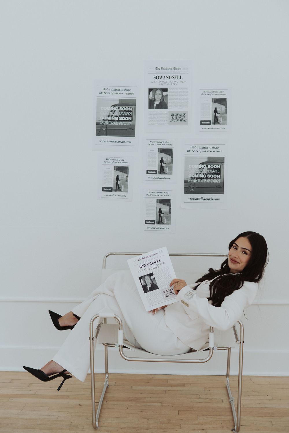 Modern white chair with newspaper clippings arranged on wall in minimalist setting.