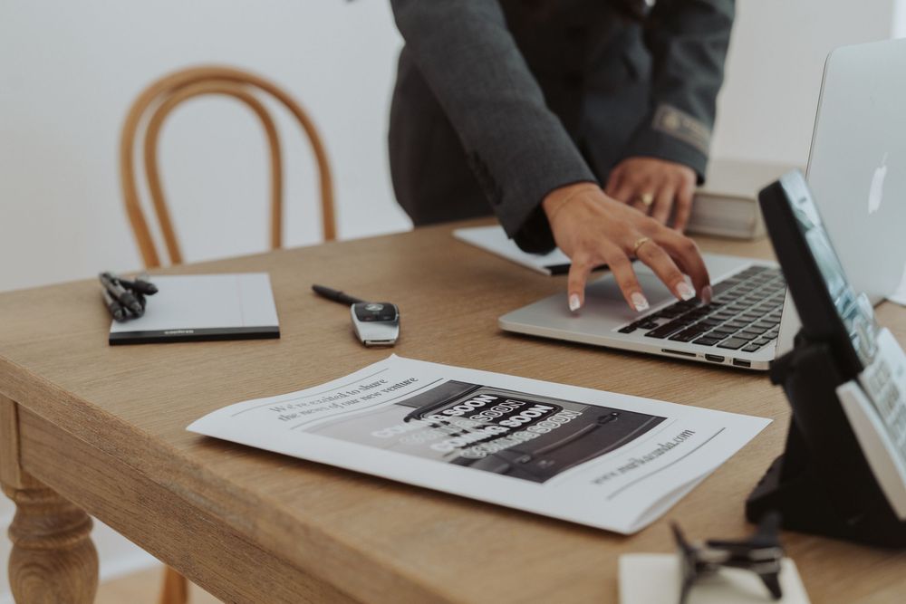 Close-up of hands working with documents and laptop on wooden desk.