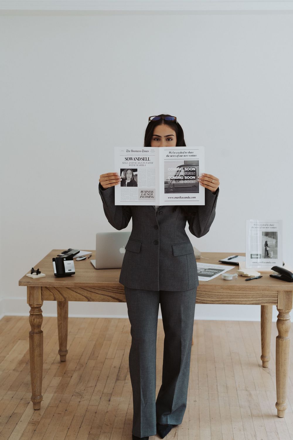 Person in grey suit standing by wooden table with business materials.