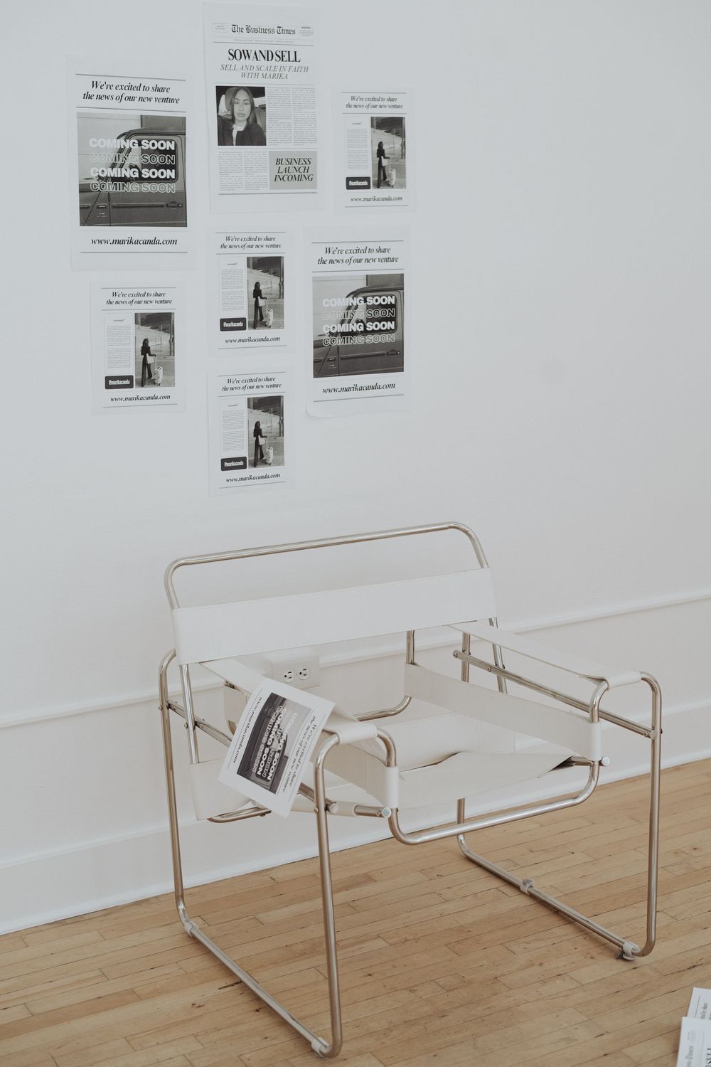 Modern white lounge chair against wall with newspaper clippings in minimalist setting.