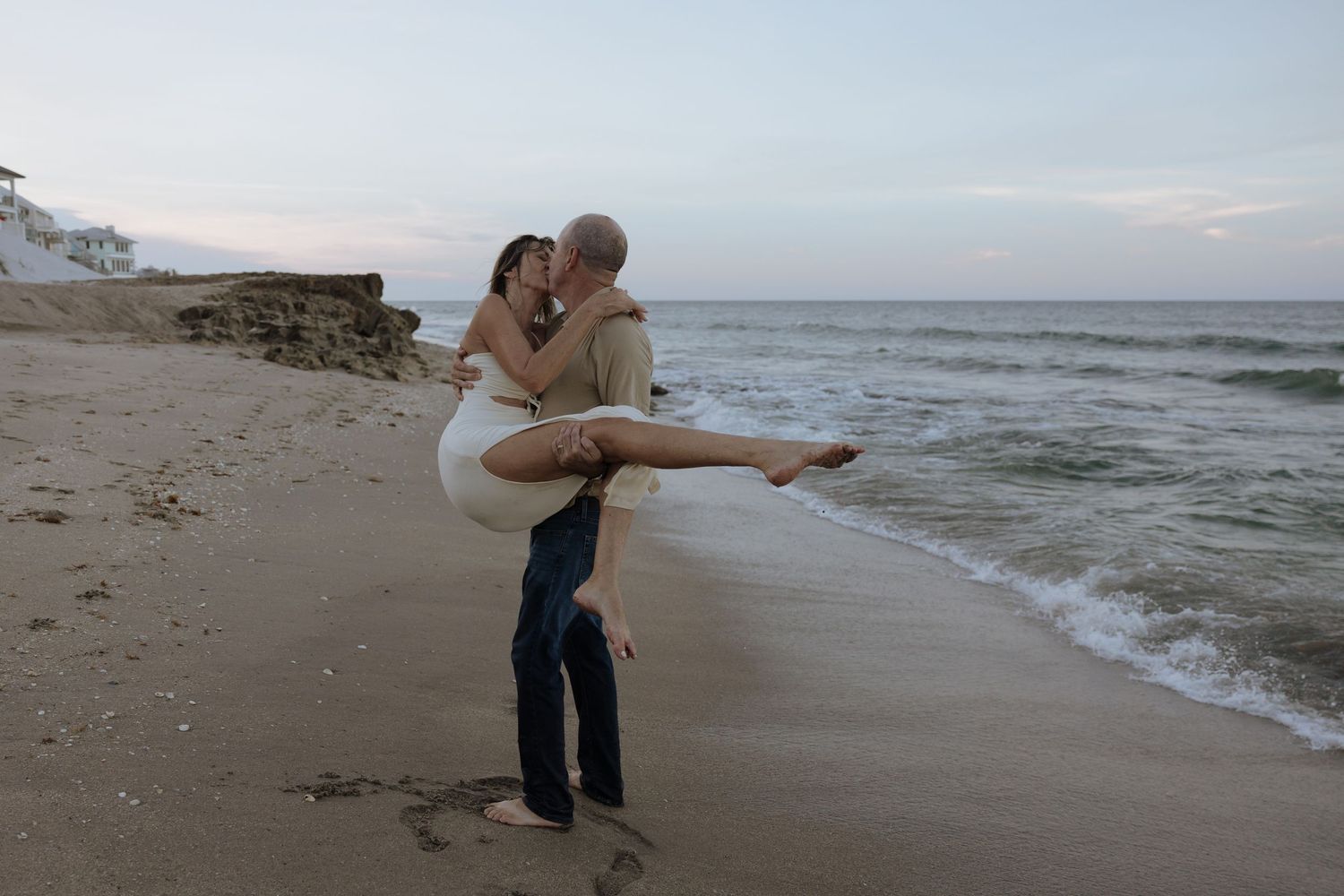 Couple walking along the shoreline of a tranquil beach during golden hour.