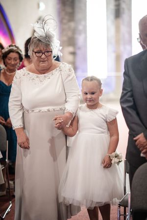 Guests in formal attire wearing white dresses gather for what appears to be a wedding ceremony in an elegant interior space.
