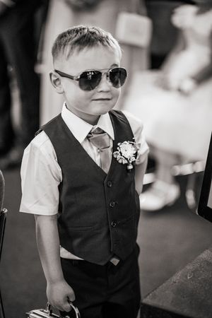 Young ring bearer in formal black vest and sunglasses looks cool in black and white wedding photography.