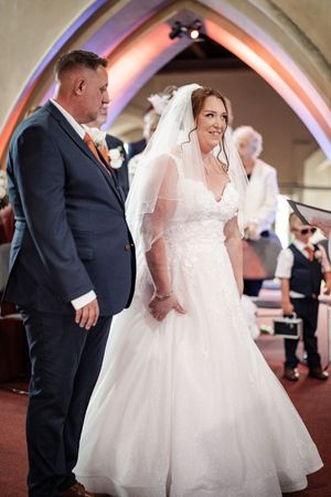 Two people share an intimate wedding dance while guests look on in an elegant arched venue with warm lighting.