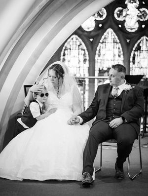 Black and white wedding photo in church with stained glass windows and gothic architecture.