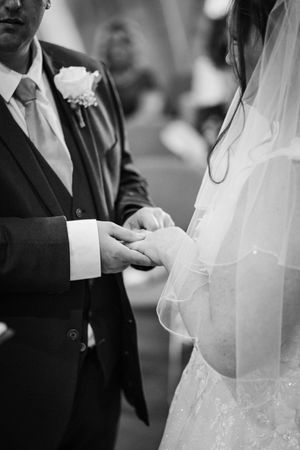 Black and white photo of a bride in a delicate white veil holding hands with someone during a wedding ceremony.