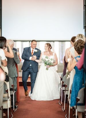 Wedding party and guests dancing and celebrating in a bright reception venue with large windows.