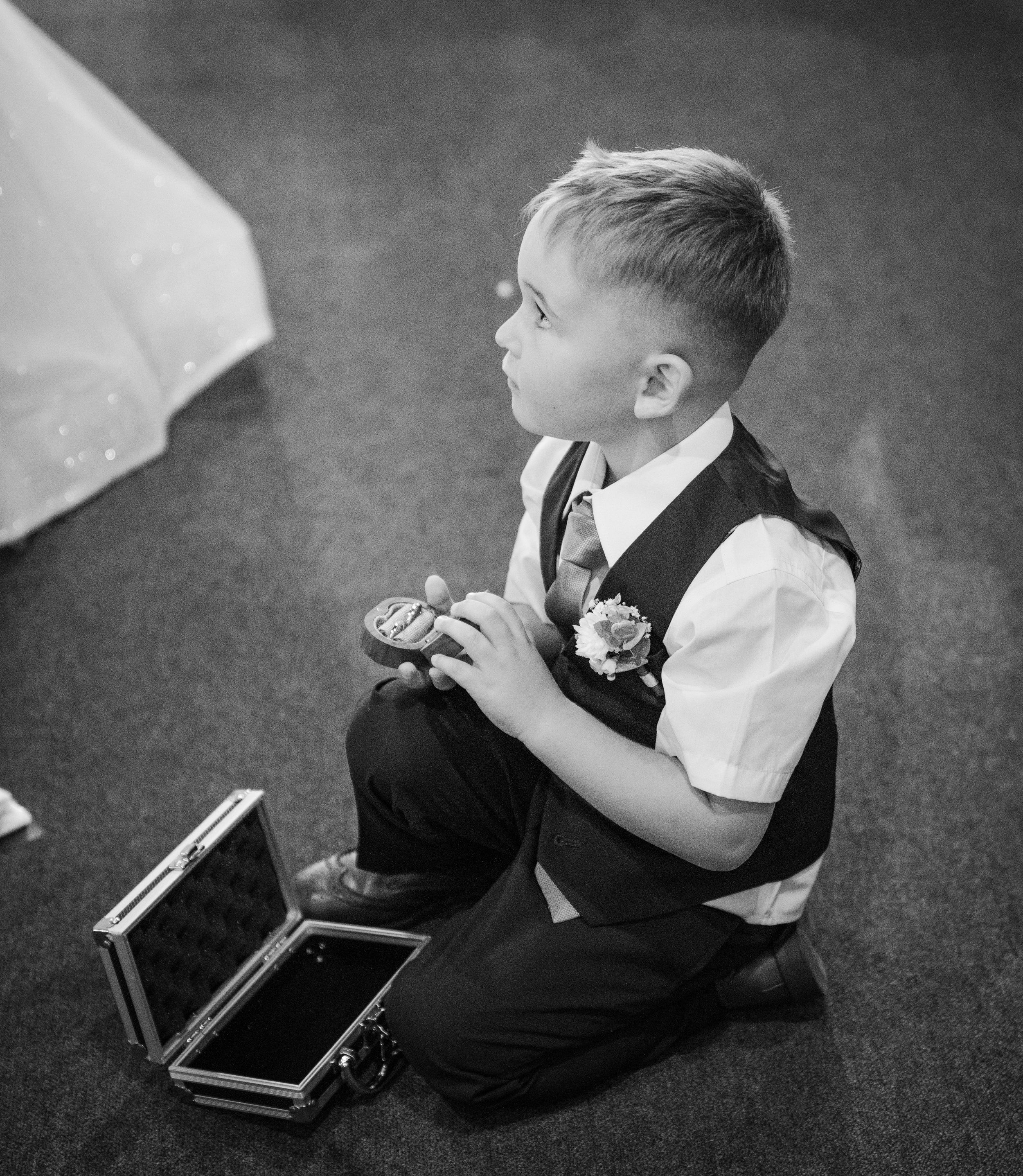 A young child kneels on the floor in formal attire while eating what appears to be a cookie or snack during an event.