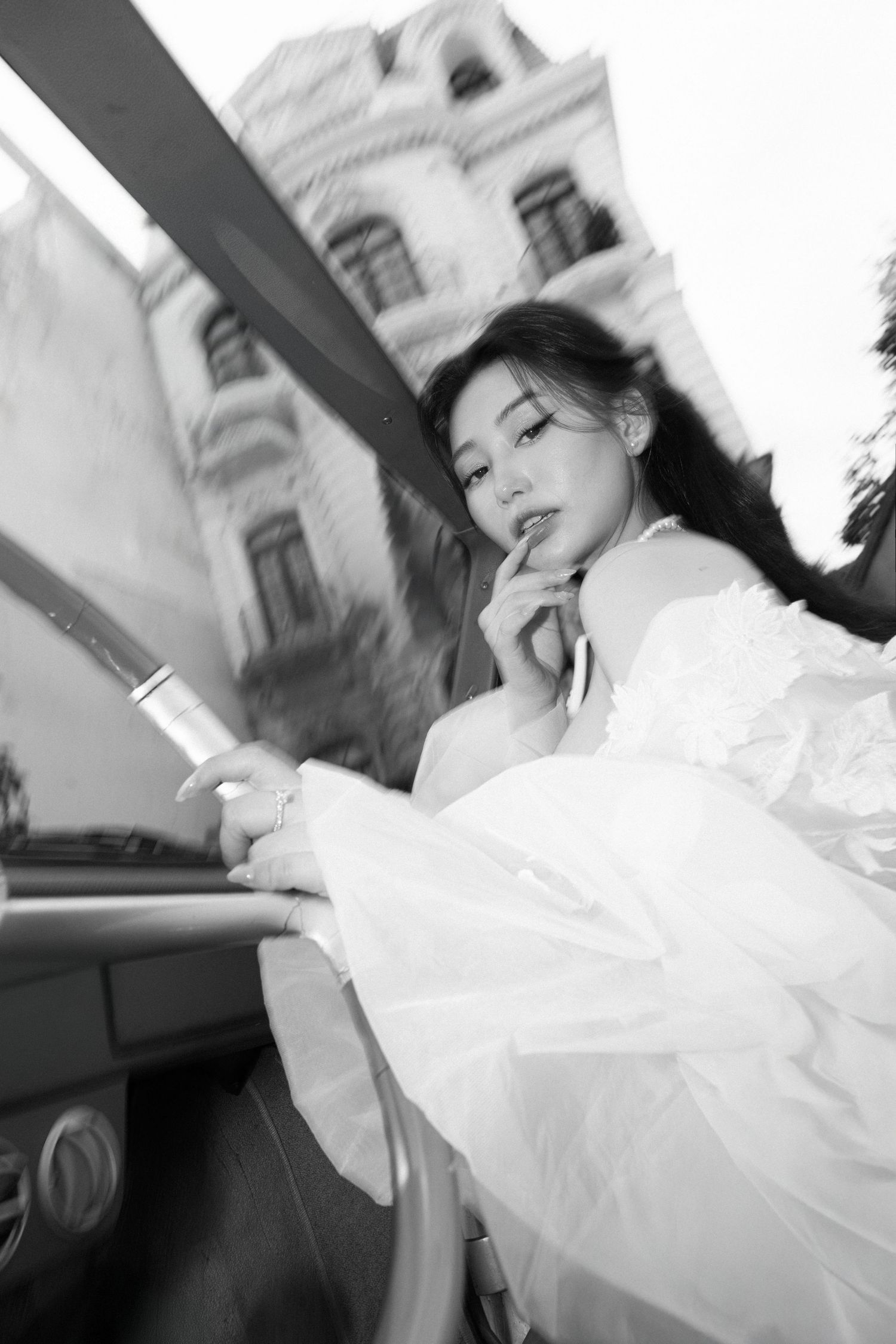 Black and white artistic photo of elegant bride in white wedding dress posing in a vintage car.