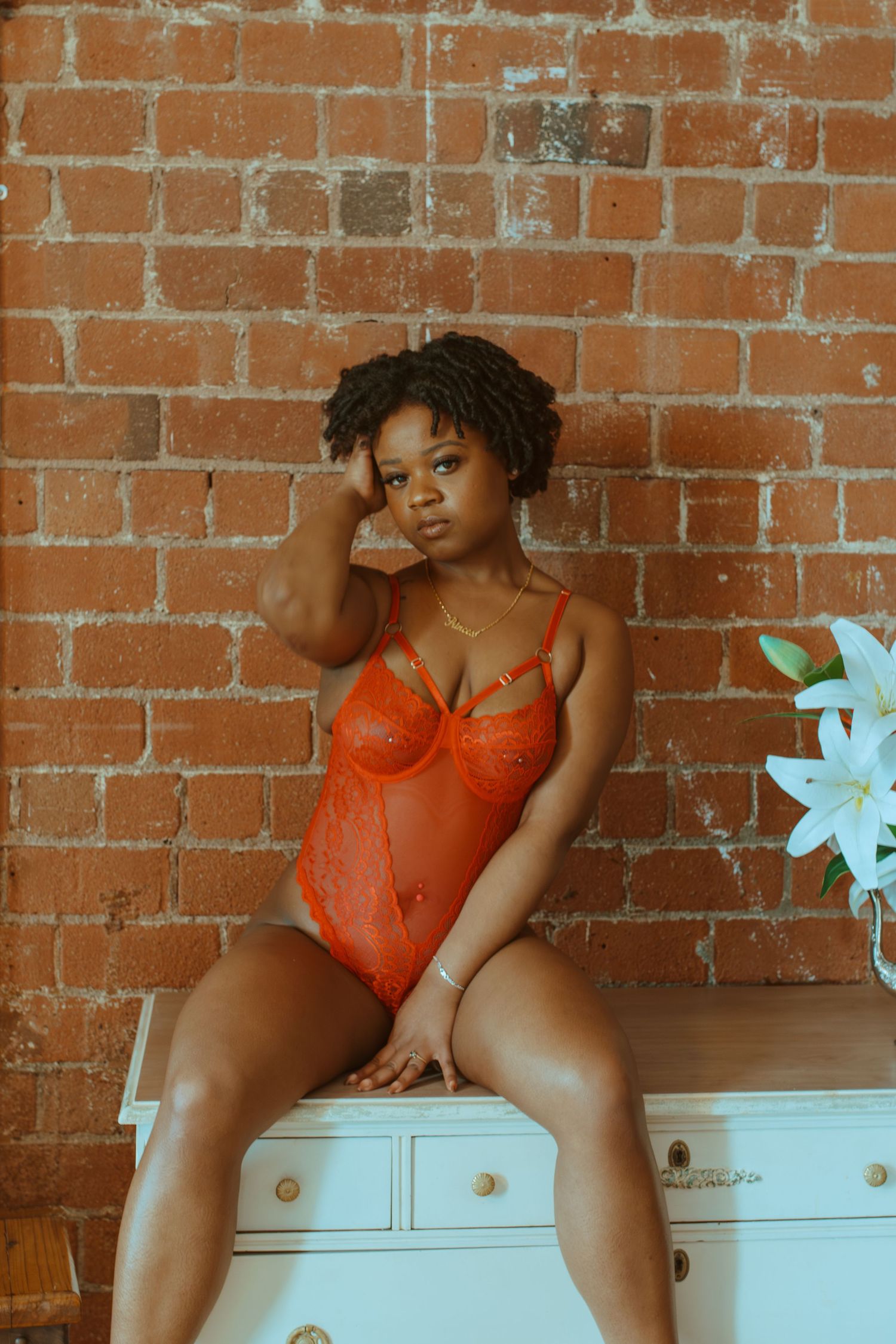 Four panels showing figure in orange lingerie posing on white furniture against exposed brick wall.
