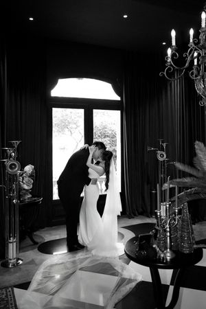 Black and white romantic photo of bride and groom sharing a kiss near large window indoors.