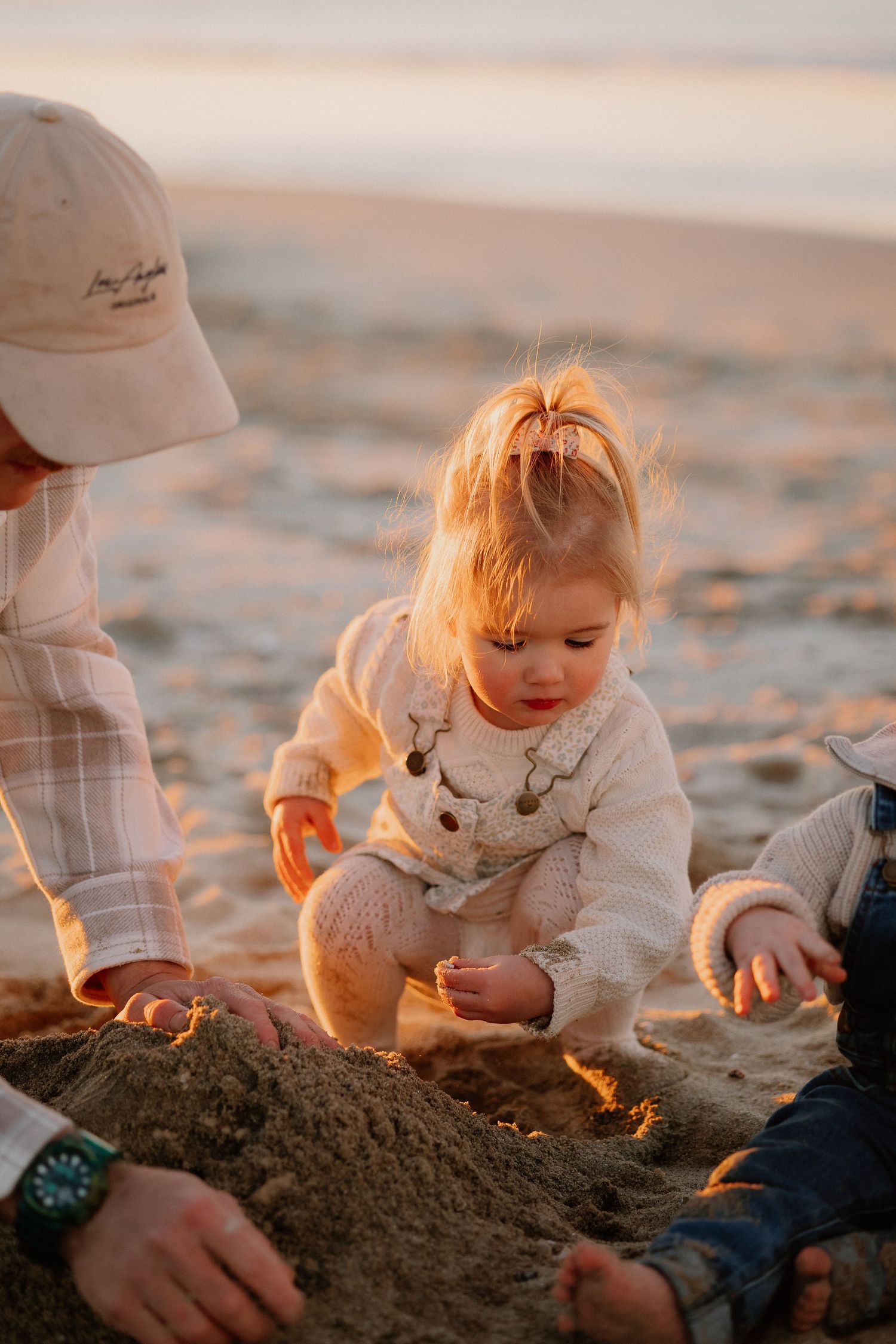 Family enjoying intimate moments together while walking on a sandy beach at sunset during golden hour.
