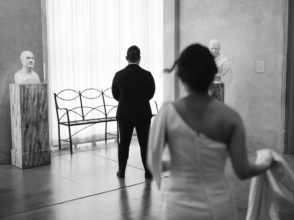 People walk through a minimalist art gallery with white walls displaying contemporary artwork and installations.