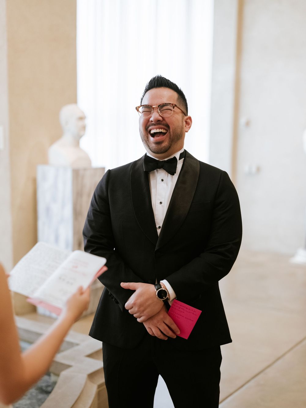 A joyful moment captured during an indoor wedding ceremony with elegant white decor and natural lighting.