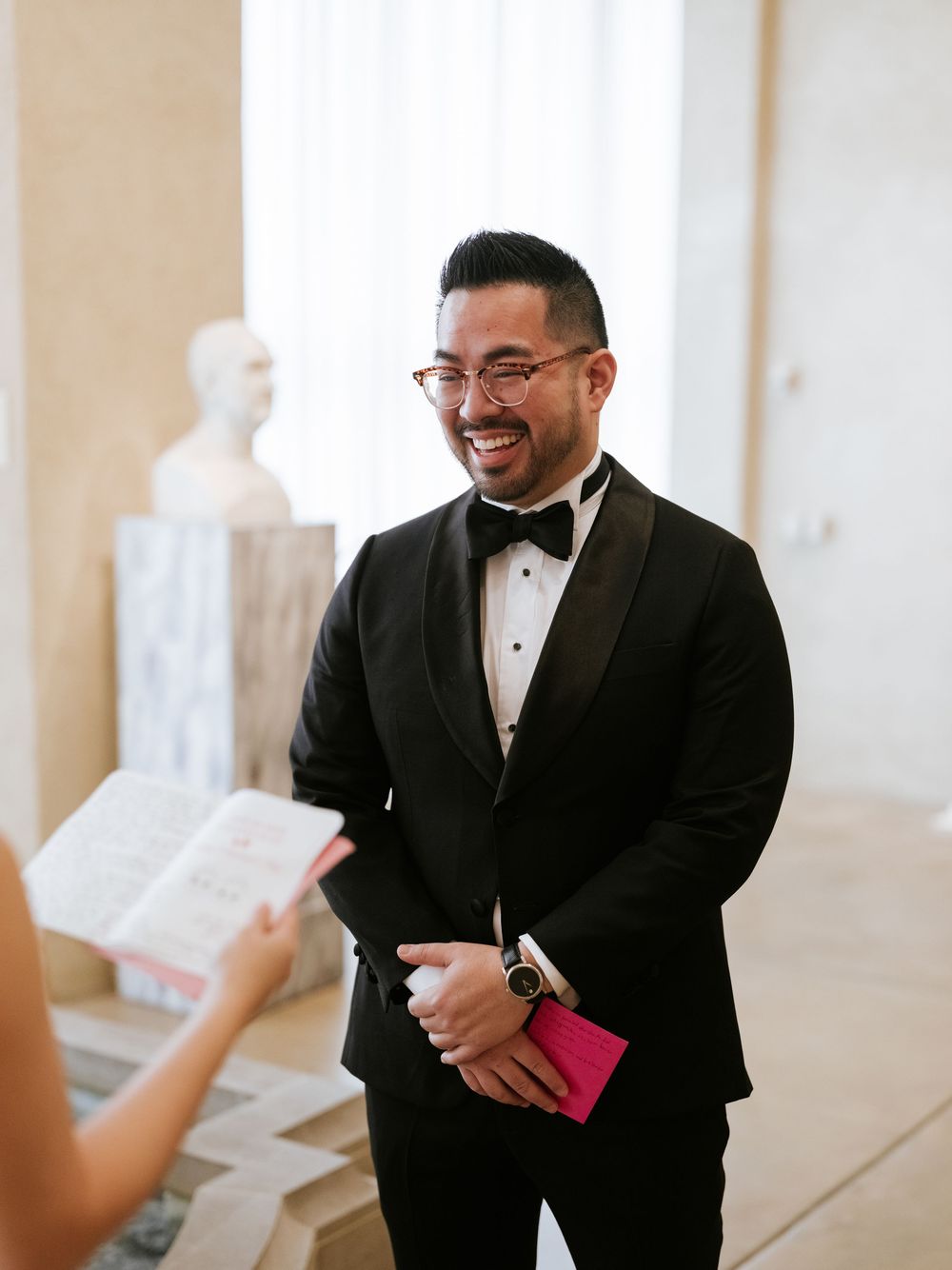 Groomsman in black tuxedo reacts emotionally while reading letter during wedding preparations.