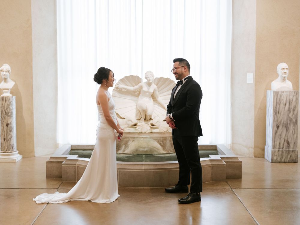 A wedding photographer captures candid moments of a bride and groom in an elegant white gallery space.