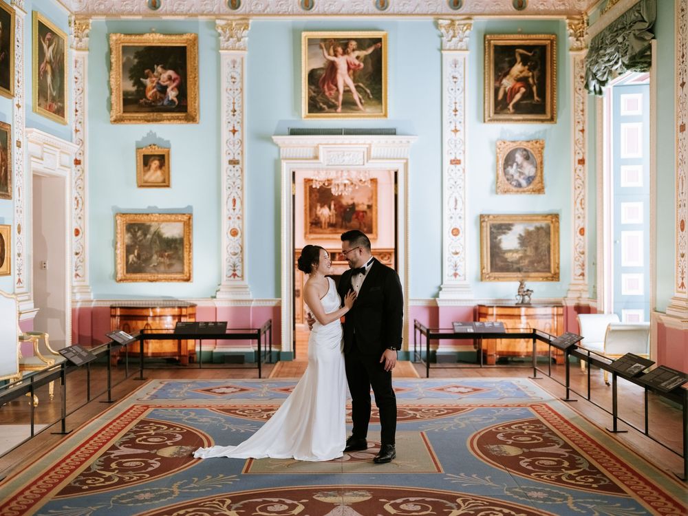 Elegant museum gallery with light blue walls showcasing classical paintings in ornate gold frames and decorative moldings.