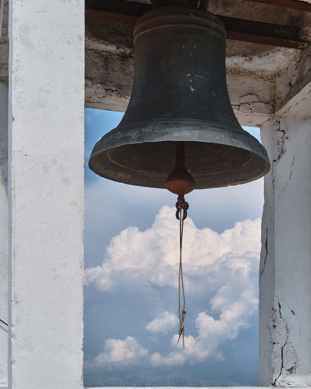 Row of large antique church bells hanging in a weathered stone bell tower against a cloudy sky.