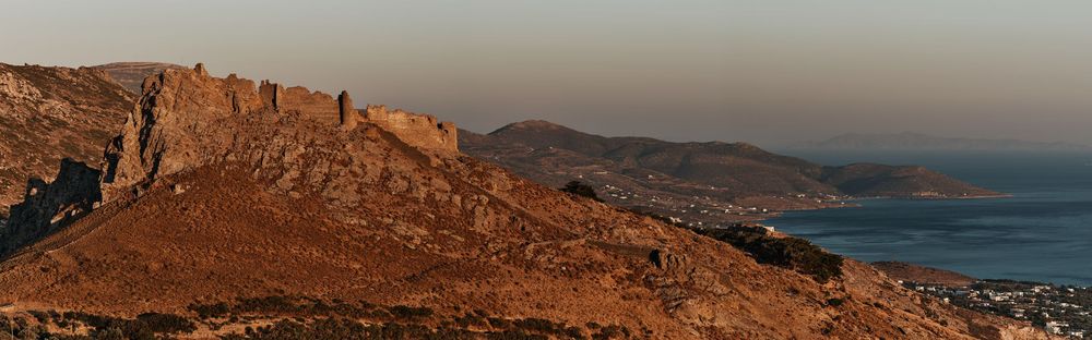 Panoramic desert landscape with mountains and coastline at sunset.