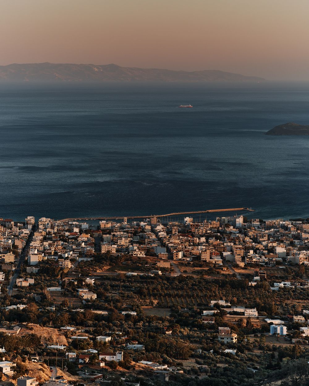 Aerial panorama of a coastal city with buildings nestled along the Mediterranean shoreline at dusk.