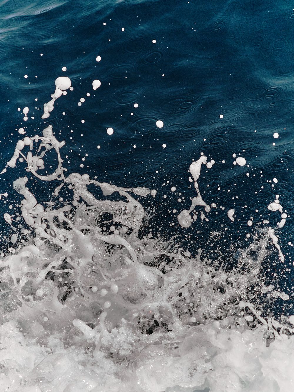 Ocean waves crash and spray white foam against deep blue water creating a dynamic splash pattern.