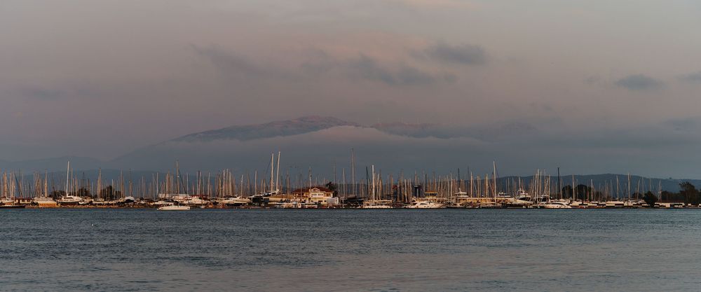 Panoramic view of a marina filled with sailboats at dusk with mountains silhouetted in the background.