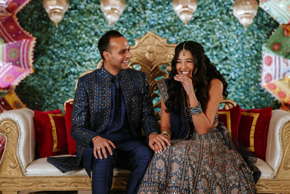 A couple shares intimate moments while sitting on elegant red chairs at what appears to be a wedding celebration.