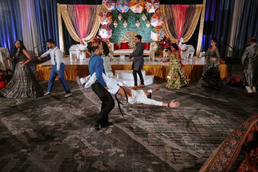 Guests dance and celebrate on a stone paved floor at a festive wedding reception with colorful decorations overhead.