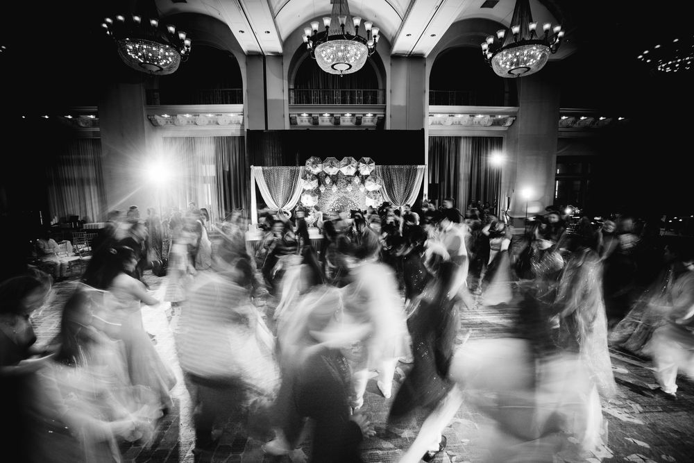 Black and white motion blur photograph of wedding guests dancing on a dark reception dance floor.