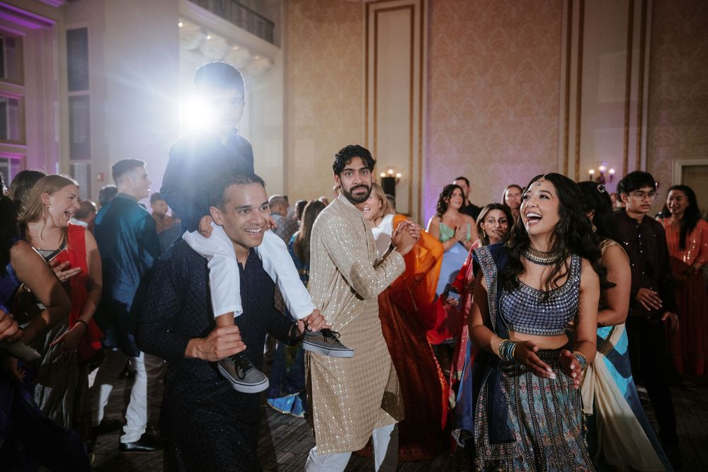 Wedding guests dancing and laughing together on a crowded dance floor at an indoor reception venue.