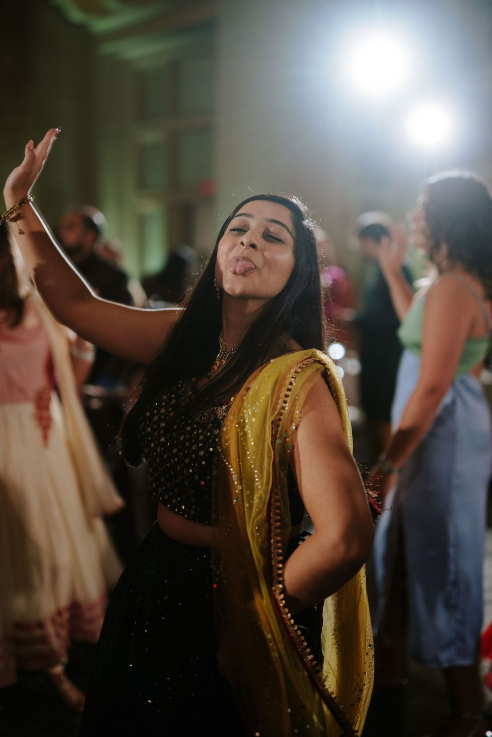 A person in a black and yellow traditional dress dances joyfully at an indoor celebration event.