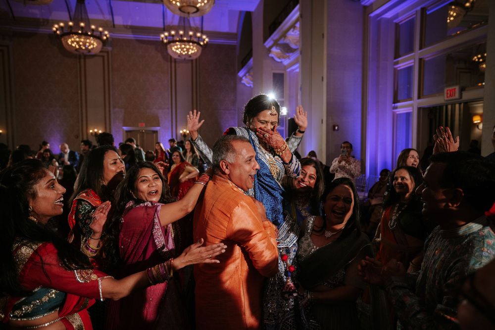 Energetic crowd dancing and celebrating at a festive event with purple lighting and chandeliers.